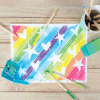 Vibrant rainbow-colored chalk art with white star and heart shapes on paper, surrounded by colorful chalk and blending tools, showcasing creative art supplies at The Wraperie.