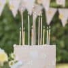 Colorful birthday candles on a white cake with floral decorations, outdoor celebration scene, festive event, lighting birthday candles, special occasion.
