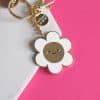 Colorful flower-shaped enamel keychain featuring a cute smiling face, perfect as a fun accessory or gift, with a white and pink background for vibrant visual appeal.