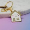 Gold house-shaped keychain with smiling face and pink cheeks, attached to gold keyring.