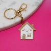 Keychain with a cute, smiling house design featuring a gold and white color scheme, perfect for home decor or gifts, on a vibrant pink background.