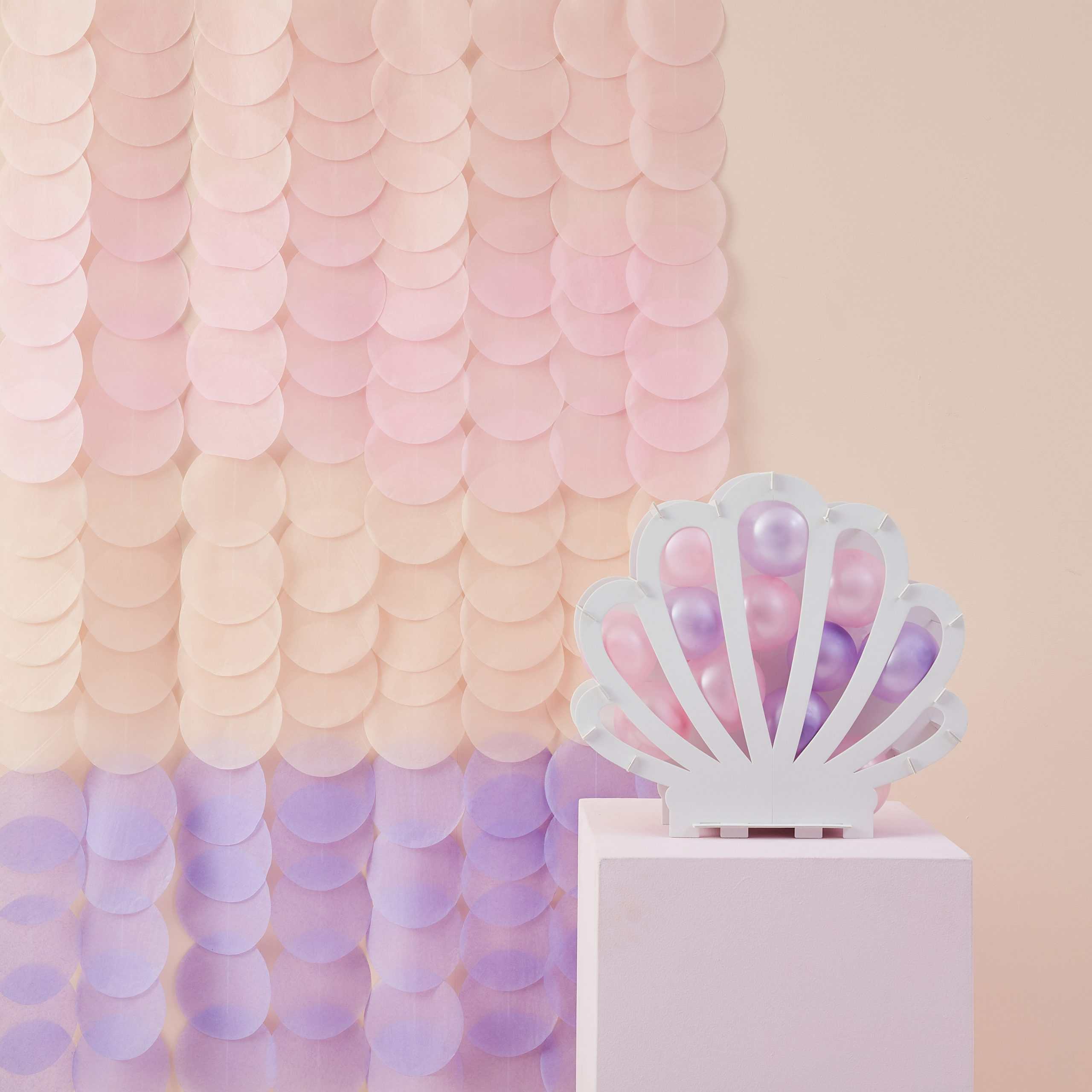 Pink and purple seashell-shaped balloon holder with pastel-colored balloons, set against a pink scalloped backdrop, creating a whimsical, beach-inspired celebration decor.