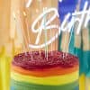 Colorful rainbow cake with lit birthday candles, sprinkles, and vibrant layers at The Wraperie for celebration and special occasions.