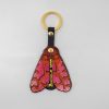 Keychain with butterfly wing embroidery, leather strap, gold hardware, vibrant pink, orange, and black colors, stylish accessory, handmade art, unique jewelry item, The Wraperie product, gift idea for fashion lovers.