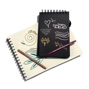 Vibrant chalkboard with colorful doodles and sketches, promoting creativity and artistic expression, placed over artistic sketchbooks with abstract drawings and markers.