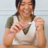 A woman smiling while holding a purple patterned toothbrush, preparing to brush her teeth, representing dental health and oral hygiene.