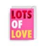 Bright pink "Lots of Love" greeting card with bold multicolored lettering, perfect for Valentine's Day and special occasions.