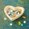 Colorful beach glass in a wooden heart-shaped dish on a rustic textured surface, perfect for beachcomber or coastal decor.