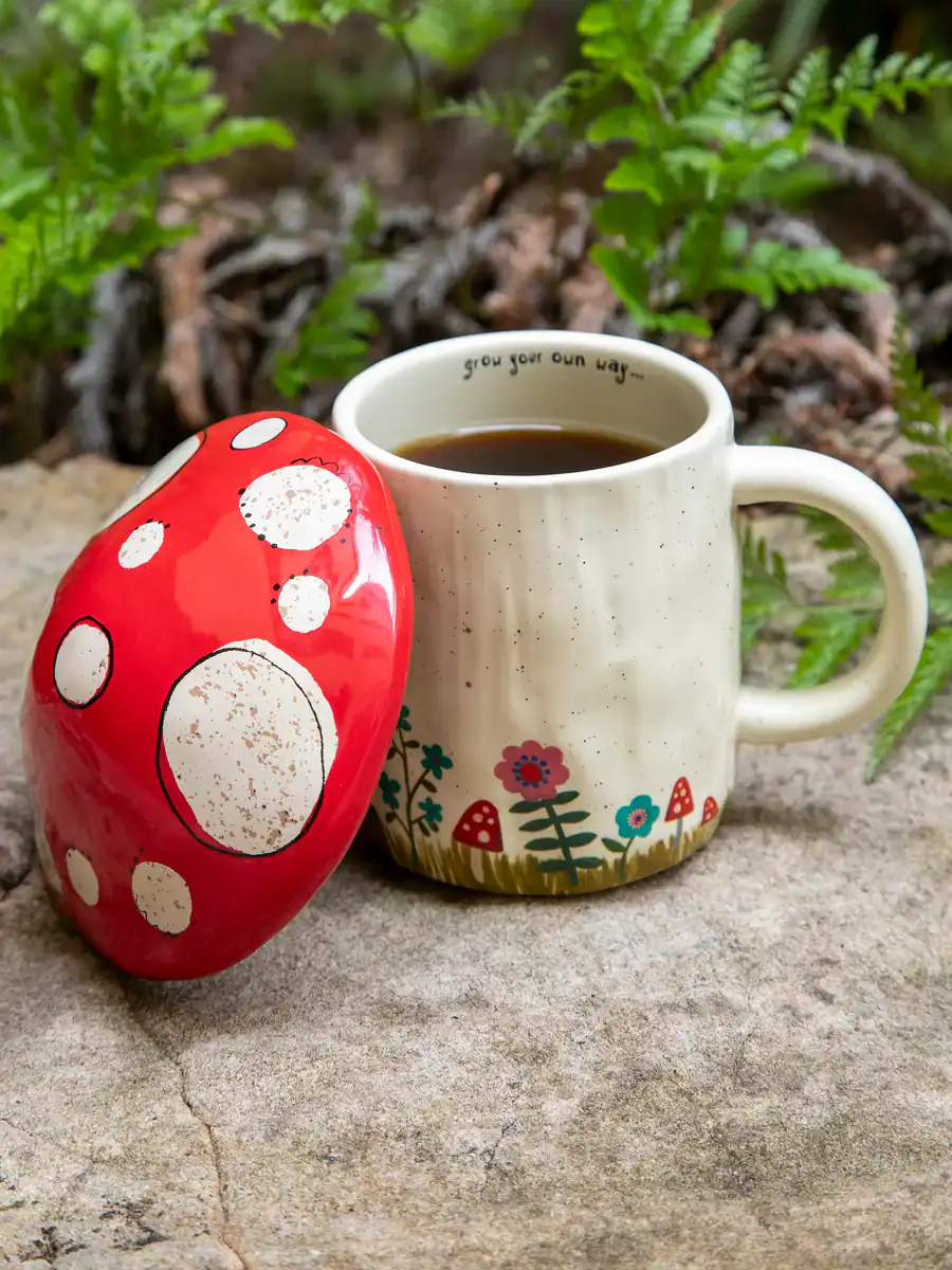 Colorful mushroom-shaped ceramic coffee mug with floral design, outdoor setting, perfect for cozy mornings, garden tea moments, whimsical kitchen decor, Nature-inspired coffee cup, The Wraperie.