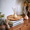 Handmade ceramic reed diffusers with natural wooden sticks on a wooden table, styled with books and fresh flowers for modern decor.