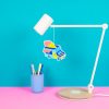 Colorful ice cream truck paper craft hanging from a white desk lamp with a blue background and pink surface, perfect for kids' craft projects and food truck themed decorations.