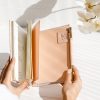 Elegant pink planner with gold accents, open to pages, served as a stylish stationary or journaling accessory. Perfect for organization, goal-setting, or creative planning.