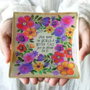 Bright floral greeting card with uplifting message "You make the world a better place just by being in it," held by a person's hands, showcasing cheerful, colorful blossoms and positive positivity themes.
