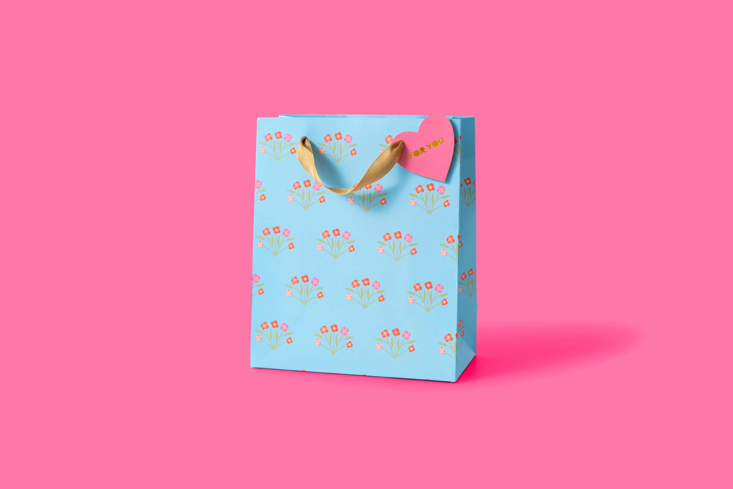 Bright blue gift bag with pink and orange floral pattern, gold ribbon handle, and pink heart tag reading "For You", perfect for special occasions and gift-giving.