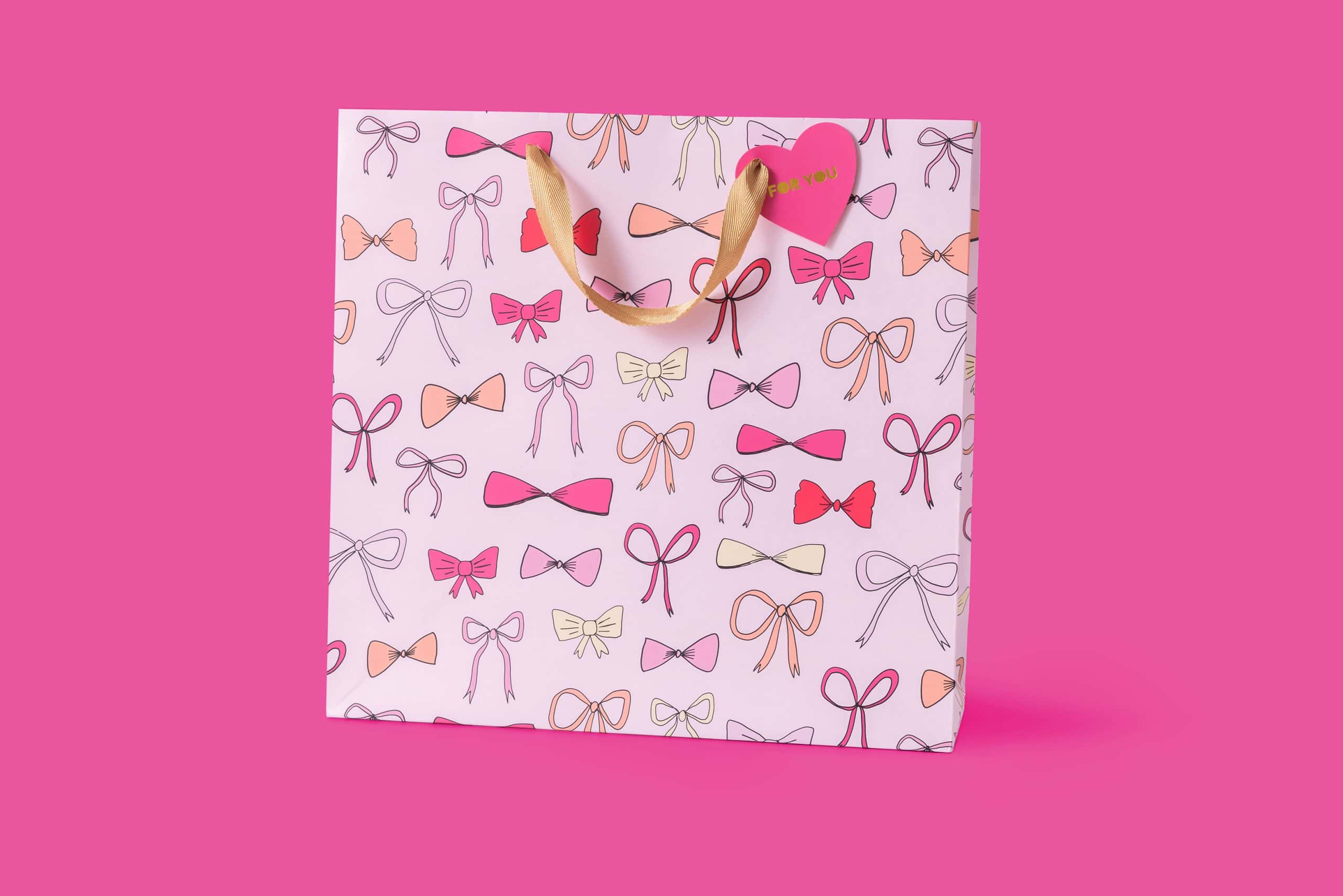 Pink gift bag with bow patterns for The Wraperie, perfect for special occasions and gift wrapping. Made with high-quality material, featuring pink, peach, and cream bows on a pastel background.