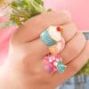 Colorful dessert-themed enamel rings on a hand with a soft pink background, perfect for fun and playful jewelry lovers seeking unique fashion accessories.