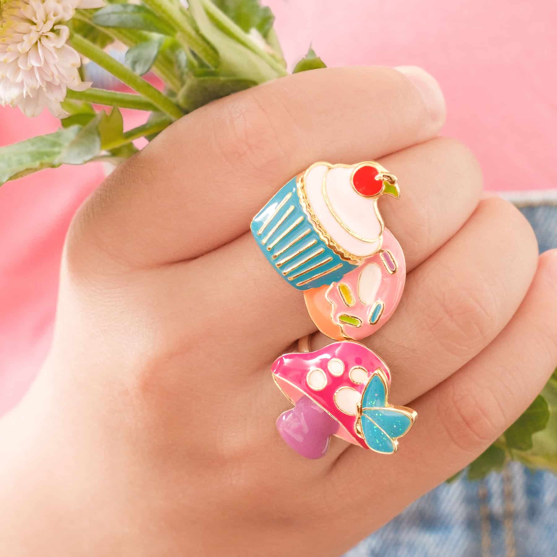 Colorful dessert-themed enamel rings on a hand with a soft pink background, perfect for fun and playful jewelry lovers seeking unique fashion accessories.