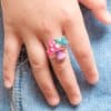 Colorful mushroom and butterfly enamel ring on a person's finger, featuring playful, artisanal jewelry designed for statement fashion accessories.