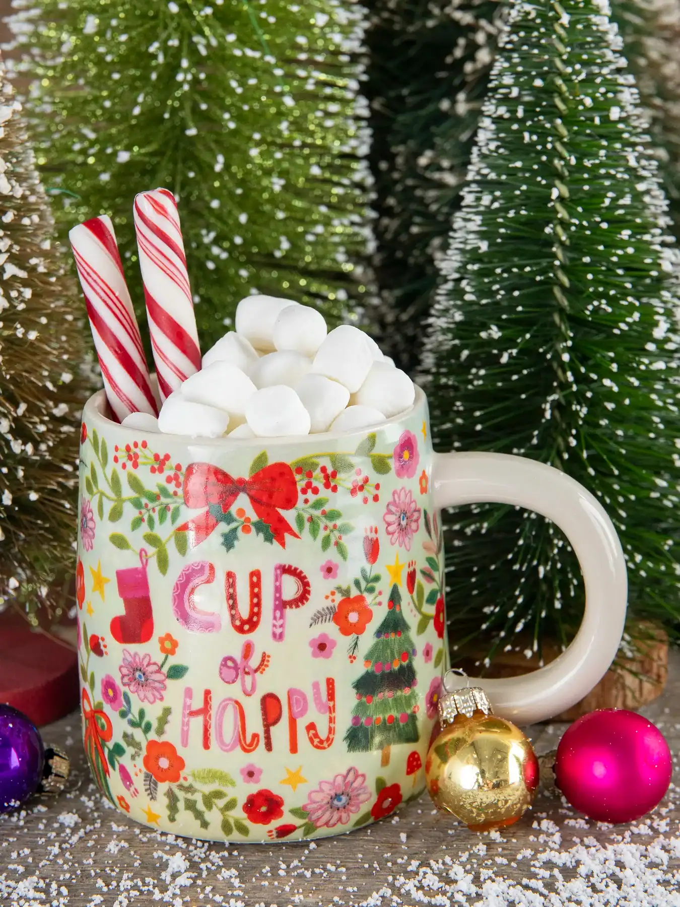 Peppermint hot chocolate mug with marshmallows, candy canes, Christmas ornaments, and festive decorations for holiday celebration.