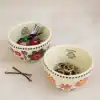 Colorful ceramic bowls filled with hair accessories and jewelry, featuring inspiring quotes, on a white surface with two hairpins nearby.
