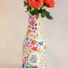 Vase with vibrant orange roses and leafy green stems against a neutral background, decorated with colorful floral patterns and the quote 