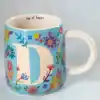 Colorful floral-designed ceramic mug with large letter "D" and "cup of happy" inside, perfect for personalized gift and coffee lovers.