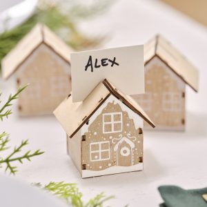 Small wooden house-shaped name card holders with the name "Alex" on one, decorative white paint details, set on a white surface for a cozy, rustic event setting.