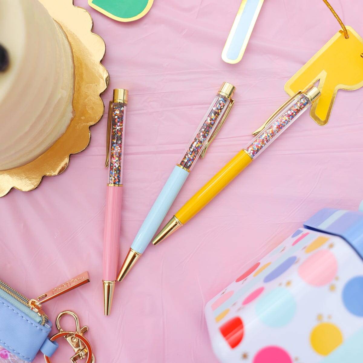 Colorful gel pens with glitter-filled barrels featuring pastel pink, blue, and yellow accents on a pink background, perfect for stationery lovers and creative office supplies.