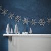 Delightful holiday decor with silver snowflake garland, miniature white Christmas trees, and a lit candle on a white mantel against a textured navy blue wall, creating a cozy festive atmosphere.