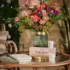 A beautiful floral arrangement with pink, purple, and yellow flowers in a modern green and gold vase serving as a centerpiece on a wooden table.