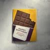 Rich, detailed dark chocolate bar with a bite taken out, decorated with a birthday message on purple and white paper, placed on a yellow background for a cheerful, festive feel.