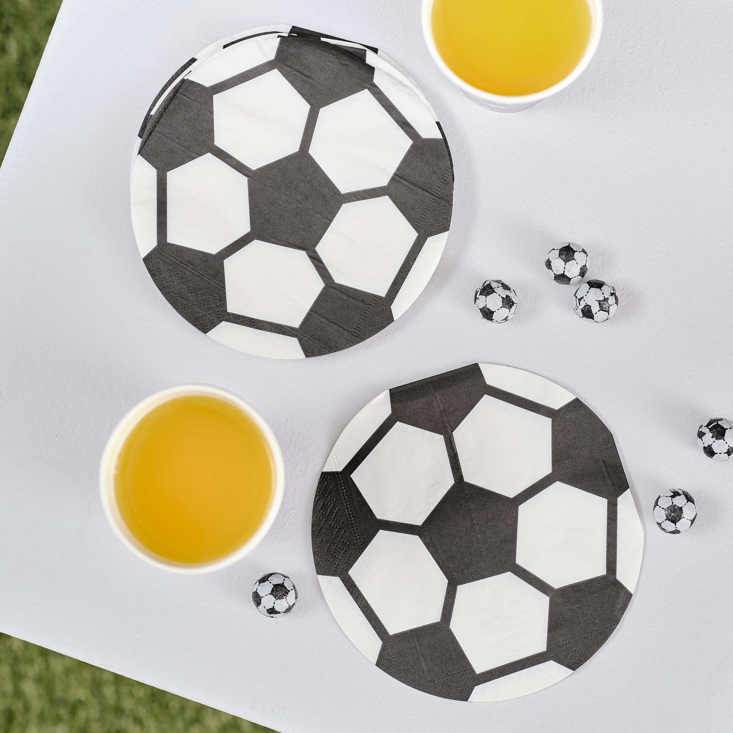Soccer-themed paper plates with black and white hexagon pattern, perfect for sports parties, along with yellow drinks and mini soccer ball decorations on a white table.