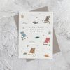 Relaxing retirement greeting card with colorful deck chairs, book, hat, coffee mug, and nature-themed elements on textured background.