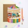 Colorful birthday greeting card featuring a carnival scene with bumper cars, a circus tent, and a "Happy Birthday" banner, perfect for festive celebrations and party decorations.