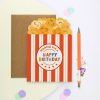 Colorful popcorn birthday card with vibrant "Happy Birthday" message, accompanied by a brown envelope and orange pen, perfect for celebrating special occasions and greeting loved ones.