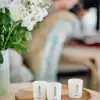 Aery scented candles on a wooden tray with a blurred background of people reading books, a floral arrangement, and soft lighting creating a cozy, relaxing atmosphere perfect for home decor or gift ideas.