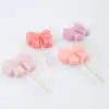 Pink bow-shaped marshmallow pops on wooden sticks, pastel-colored sweet treats, perfect for parties and celebrations, cute desserts for kids and adults, The Wraperie specialty confections, vibrant and Instagram-worthy.