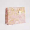 Vibrant pink and gold marble-patterned gift bag with cream-colored handles, perfect for stylish gift presentation.