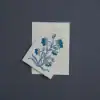 Delicate blue floral embroidered design on white fabric napkin, perfect for table settings or gifting, showcasing intricate craftsmanship and vibrant color details.