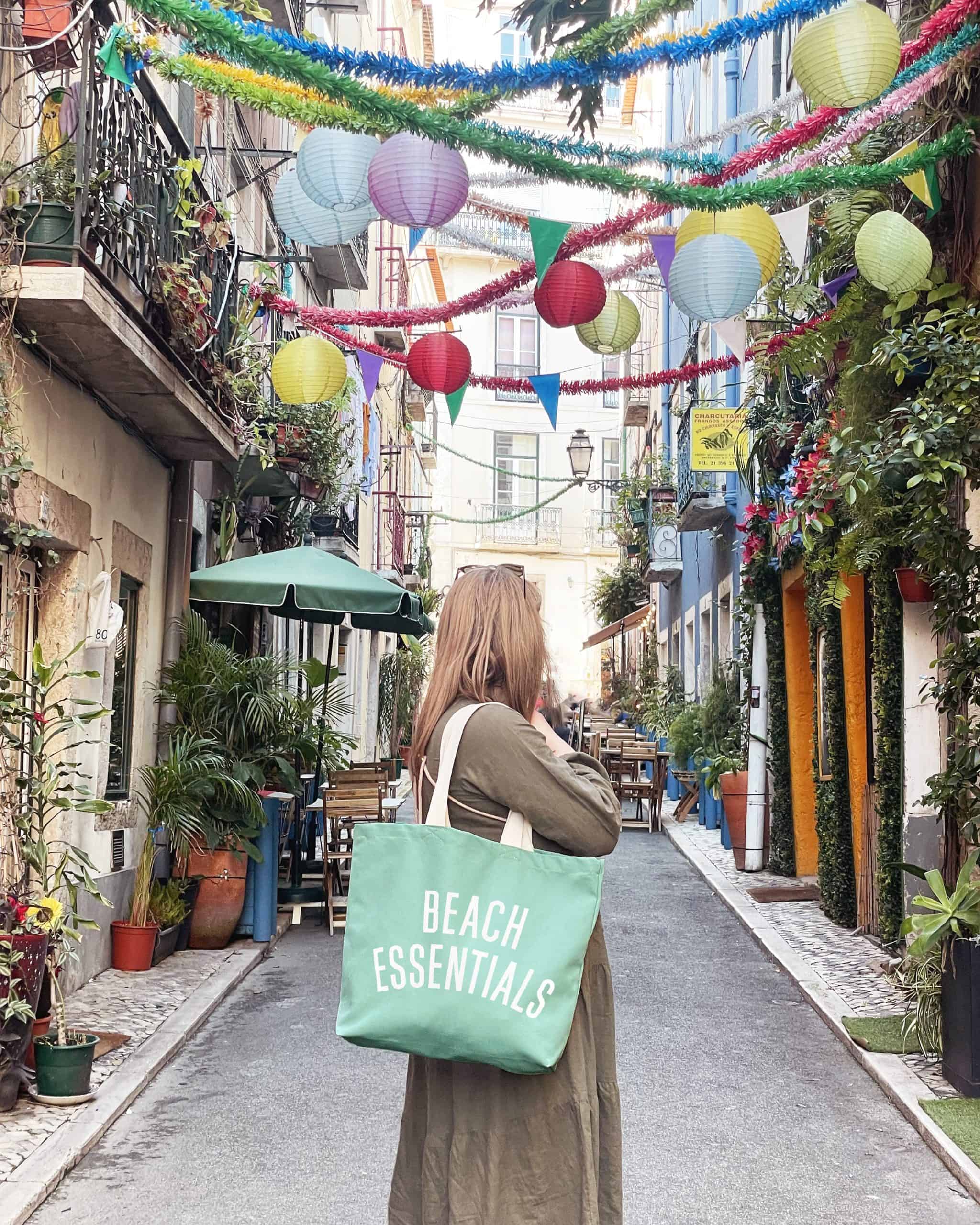 Beach essentials tote bag in a charming outdoor urban cafe setting with colorful decorations and vibrant plants, perfect for summer beach outings and seaside adventures.