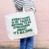 Positive message tote bag with motivational quote, casual outfit, standing against pink wall, promoting wellness, self-care, and positivity.