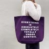 Purple tote bag with bold white text, woman wearing cozy sweater, casual fashion accessory, grocery shopping, The Wraperie, custom tote, reusable shopping bag, stylish eco-friendly tote bag, promotional tote design, retail tote bag for branding.