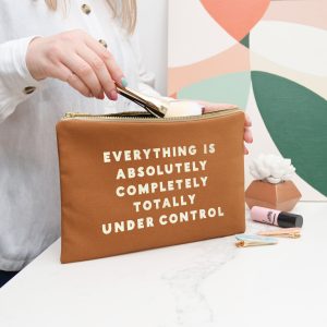 Aesthetic cosmetic bag with motivational quote, beauty products, and makeup tools on a white marble surface.