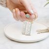 Colorful nail polish on hand holding gold keychain with inspirational words, on white ceramic plate, showcasing custom jewelry from The Wraperie.