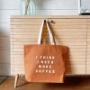 Vegan tote bag with coffee quote hanging on wooden cabinet in modern café decor.