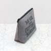 A stylish grey pouch with a motivational quote, perfect for storing small essentials, on a white marble surface.