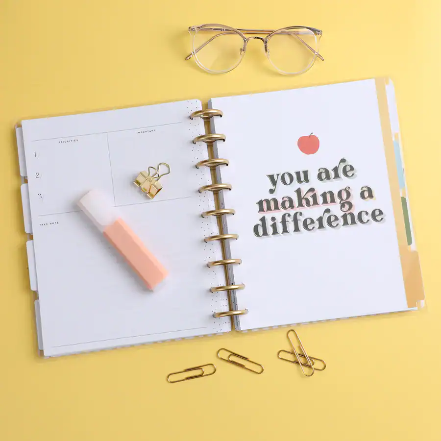 "Planner with motivational message 'you are making a difference' on a yellow background, with office supplies, glasses, and decorative paper clips".