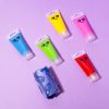 Colorful gel toothpaste tubes with cute face designs on pastel purple background, representing fun and innovative oral care products from The Wraperie.