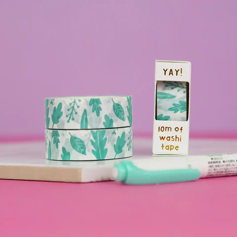 Colorful washi tape rolls with leaf patterns and a small box of decorative tape on a pink background, perfect for crafting and gift wrapping.