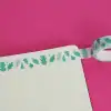 Colorful leaf-patterned washi tape on white paper against pink background, used for decorative crafts and stationery embellishments.